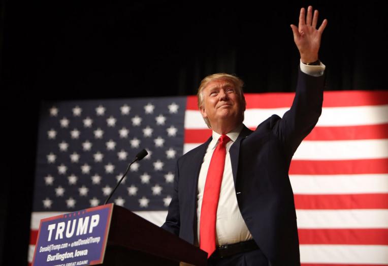 Trump waving in front of flag